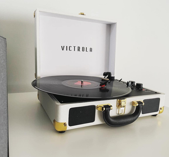 Reviewer image of white and black suitcase turntable with two black dials and a black record spinning on top of a white table