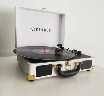 Reviewer image of white and black suitcase turntable with two black dials and a black record spinning on top of a white table