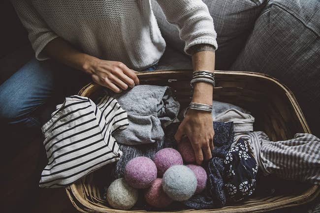 model placing clothes into a wicker basket with wool dryer balls