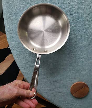 reviewer holding a shiny metal pan that was cleaned using the dawn dish spray