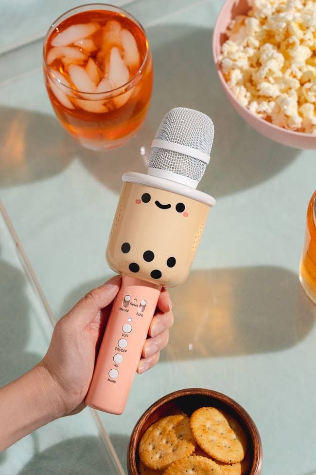 hand holding wireless mic with volume and echo controls, pink handle, and bubble tea character at the top of the handle