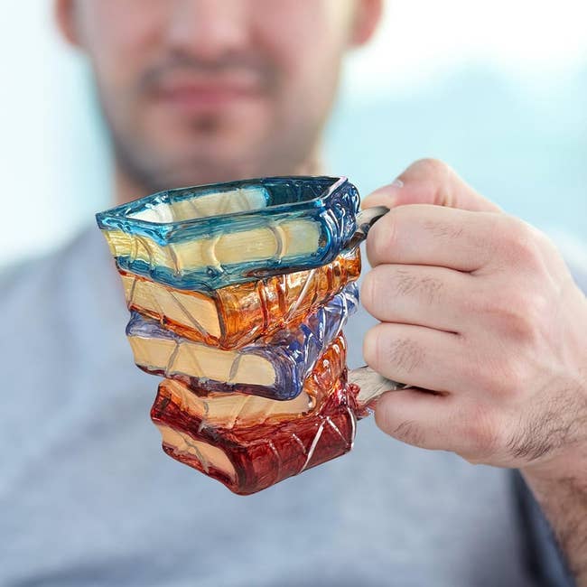 Person holding a stack-of-books-shaped mug, creating an eye-catching illusion of books arsenic  a mug