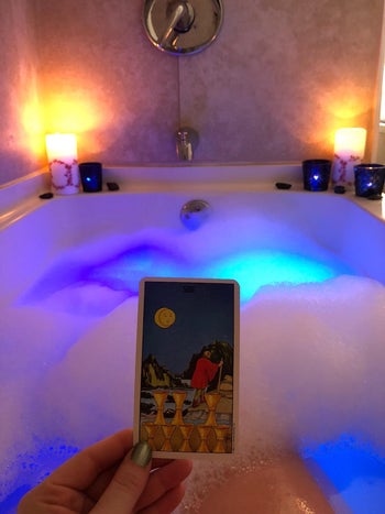 reviewer photo of them holding a tarot card over a bubble bath being lit blue and purple
