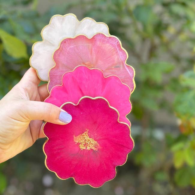 Hand holding 4  scalloped-edge coasters successful  varying shades of pink, with golden  trim, successful  a plot  setting