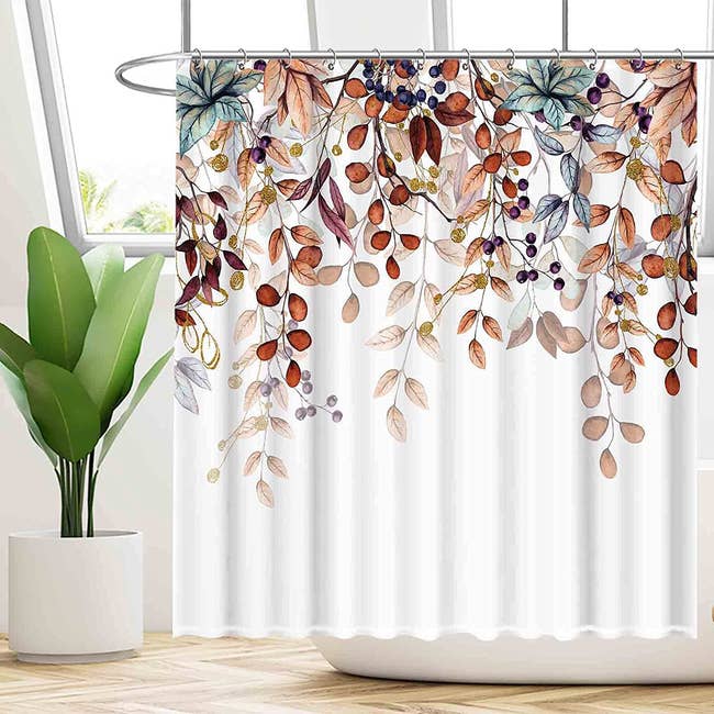 the white shower curtain with orange, brown, and otherwise autumnal-looking leaves draping down from the top of it