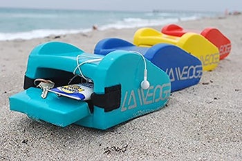 three wedge pillows on the beach with the storage compartment open holding a bottle of sunscreen, headphones, and keys