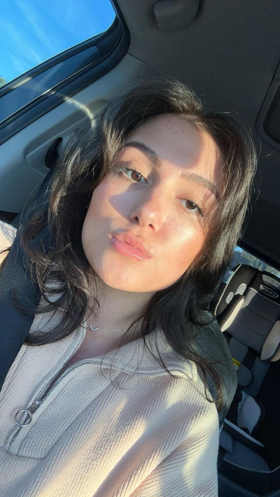 Person taking a selfie successful  a car, wearing a zip-up casual top, with airy  falling connected  their face