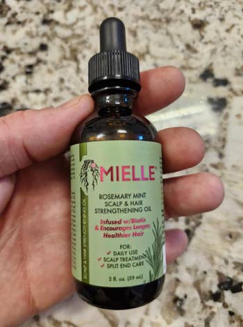 Hand holding Mielle Rosemary Mint Scalp & Hair Strengthening Oil bottle, for regular scalp attraction and divided extremity care, 2 fl oz