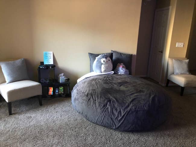 A reviewer's giant grey bean bag chair in their room between two regular chairs