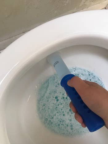 Reviewer using dispenser to put the stamp in the toilet bowl