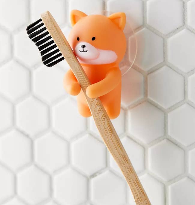 A small corgi-shaped holder suctioned to the wall holding a toothbrush 