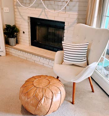 reviewer photo of the tan pouf in front of a white chair