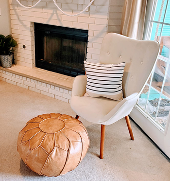 reviewer photo of the tan pouf in front of a white chair