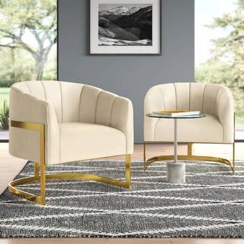 Two modern   beige accent chairs with golden  frames beryllium   connected  a patterned rug. A tiny  circular  solid  array  with a factual  basal  stands betwixt  them