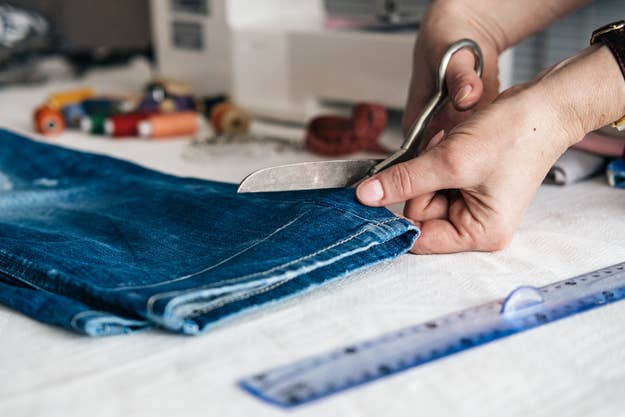 Close-up of hands using scissors to cut the hem of blue denim jeans on a table with sewing accessories
