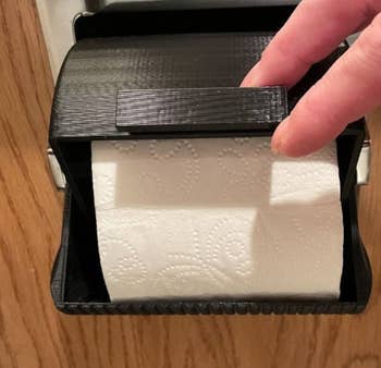 A toilet paper roll inside a black protector that prevents it from being unraveled by pets 