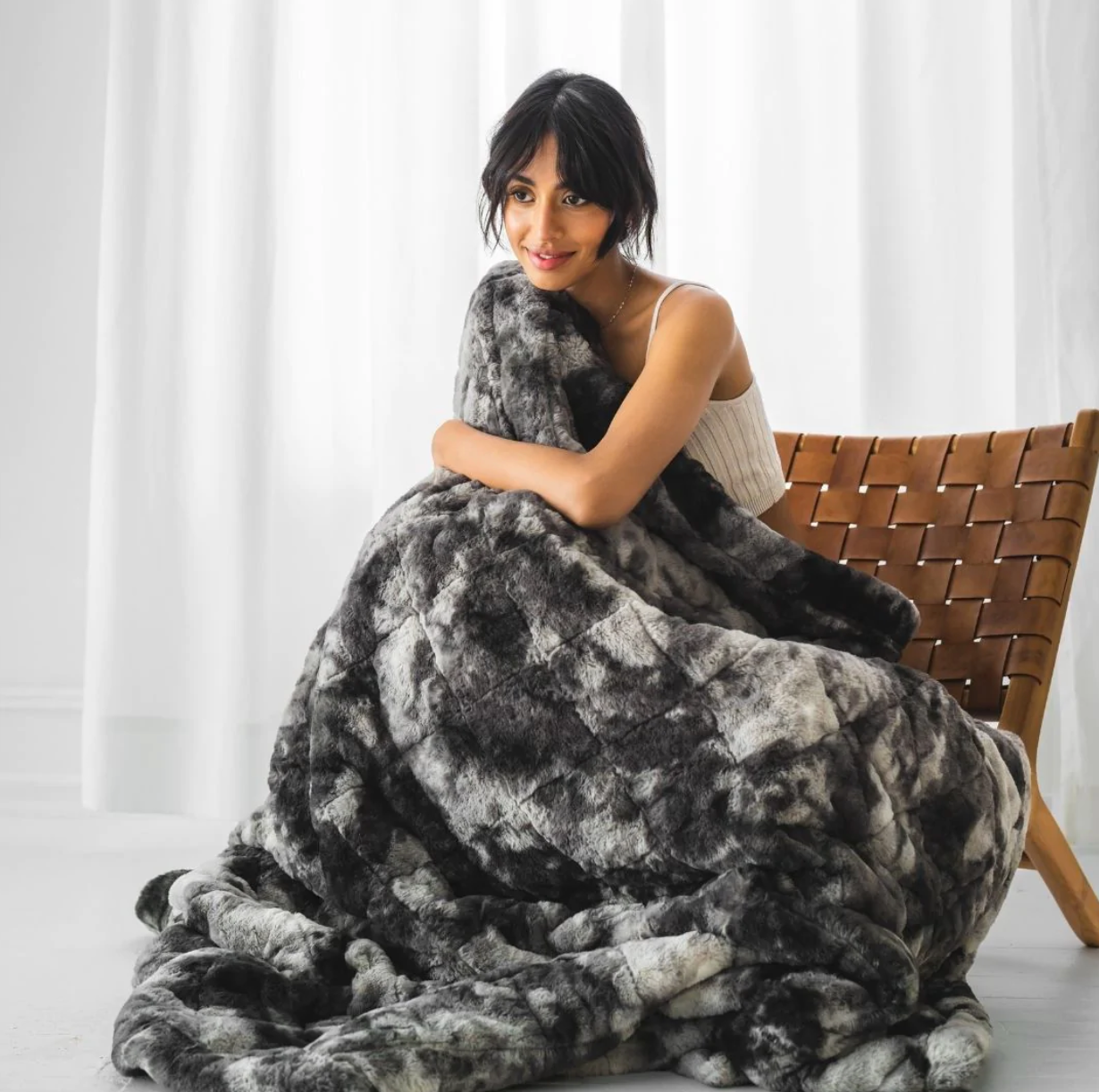 Model snuggling a gray faux fur weighted blanket 
