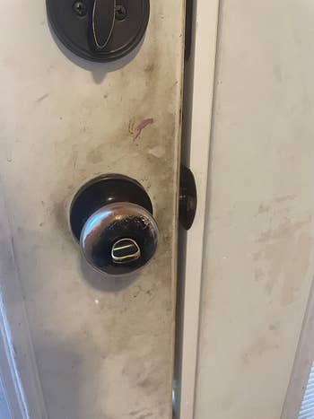 A close-up of a worn doorway  with a scratched doorknob and marks, somewhat  ajar, showcasing location  introduction  condition