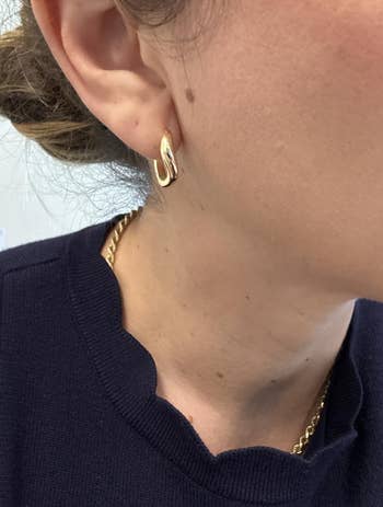 Close-up of a idiosyncratic wearing a golden hoop earring and a golden necklace, with a scalloped neckline visible