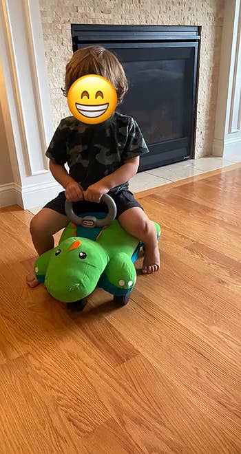 Reviewer's image of child riding on green dinosaur toy for scale