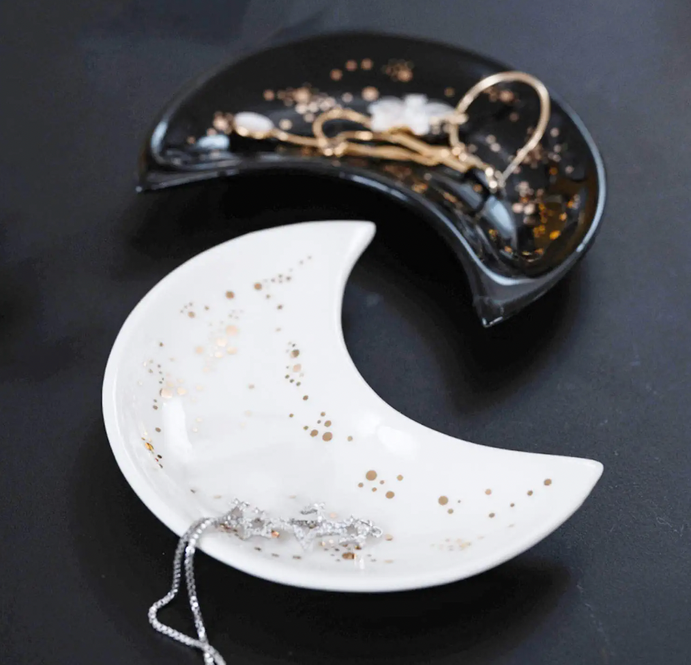 Two half moon trinket trays, one black and one white, with gold speckle detall 