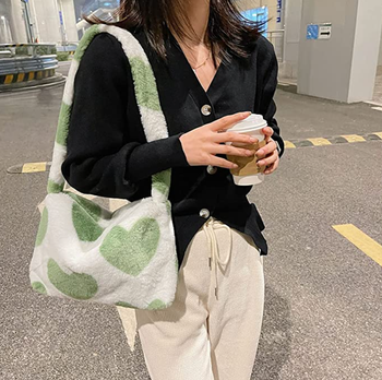 person walking while wearing green heart bag and holding a coffee
