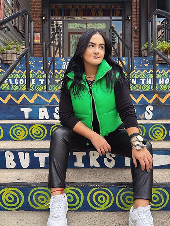 reviewer wearing the green vest with a black top, pants, and white sneakers