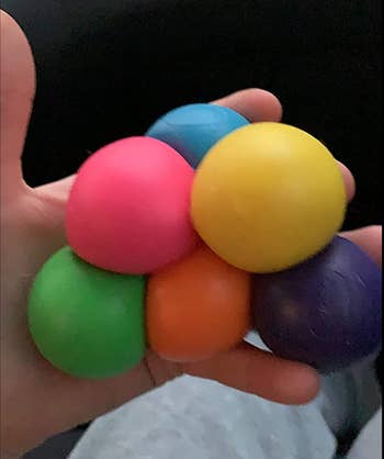 Reviewer holding six squishy balls in different rainbow colors in their hand 