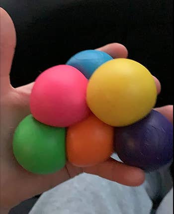 Reviewer holding six squishy balls in different rainbow colors in their hand 