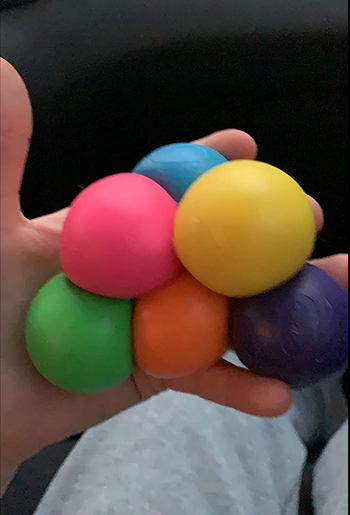 Reviewer holding six squishy balls in different rainbow colors in their hand 