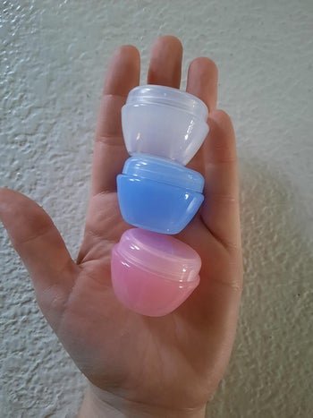 reviewer holding three small travel storage tubs in assorted colors