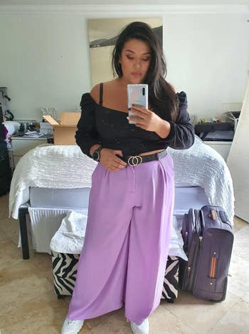 Person in puff-sleeve top and high-waisted purple trousers with belt, taking a mirror selfie