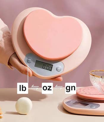 Person using a heart-shaped kitchen scale to weigh an ingredient; scale displays digital reading