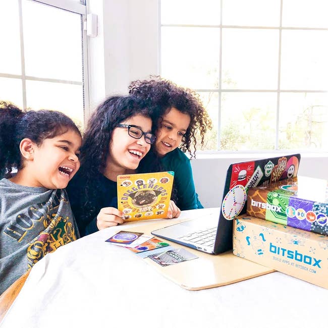 three children laughing while sitting around a laptop