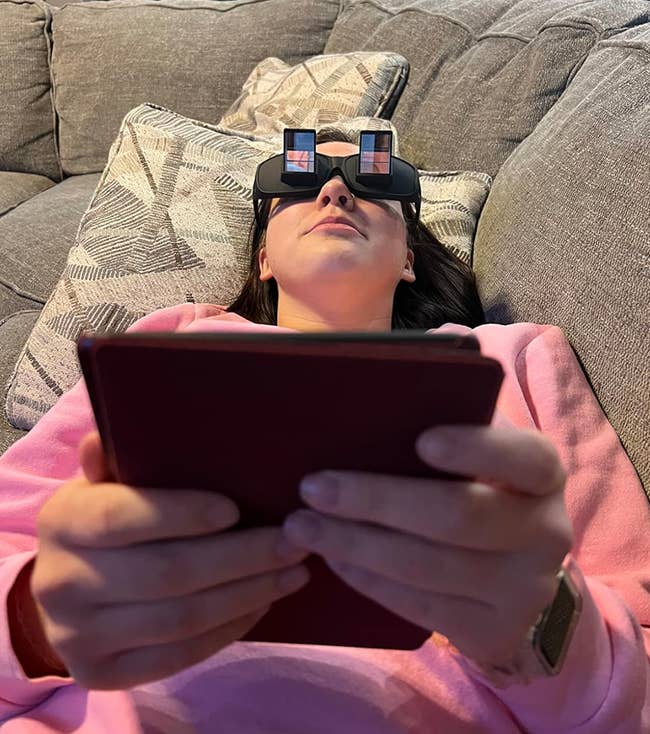 Reviewer laying on the couch while reading a book upright using the glasses 