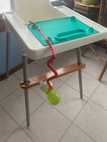 High chair with a green tray, a red sippy cup secured by a strap to avoid spills on the floor. 