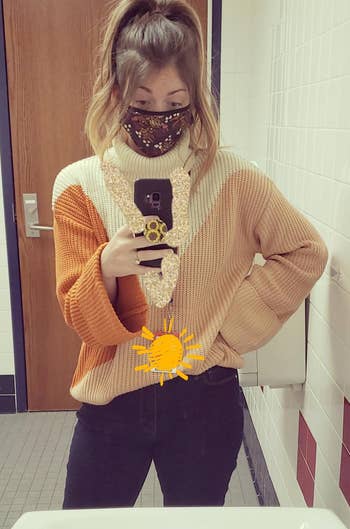 reviewer taking a mirror selfie while wearing the brown and orange sweater