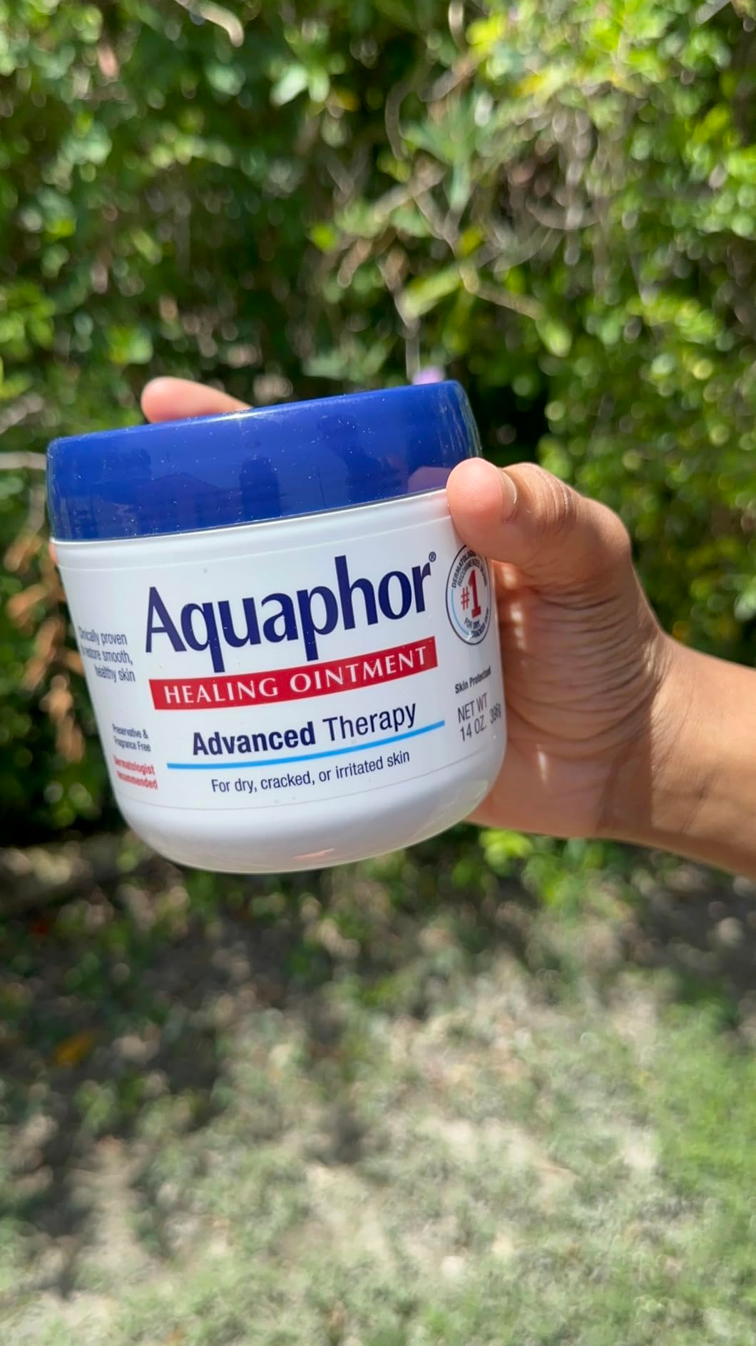 A manus  holding a jar of Aquaphor Healing Ointment against a leafy background. The statement   highlights its usage  for dry, cracked, oregon  irritated skin