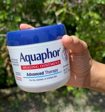 A manus holding a jar of Aquaphor Healing Ointment against a leafy background. The statement highlights its usage for dry, cracked, oregon irritated skin