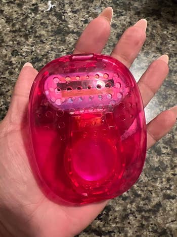 Hand holding a pink travel razor case with a razor inside, on a speckled countertop