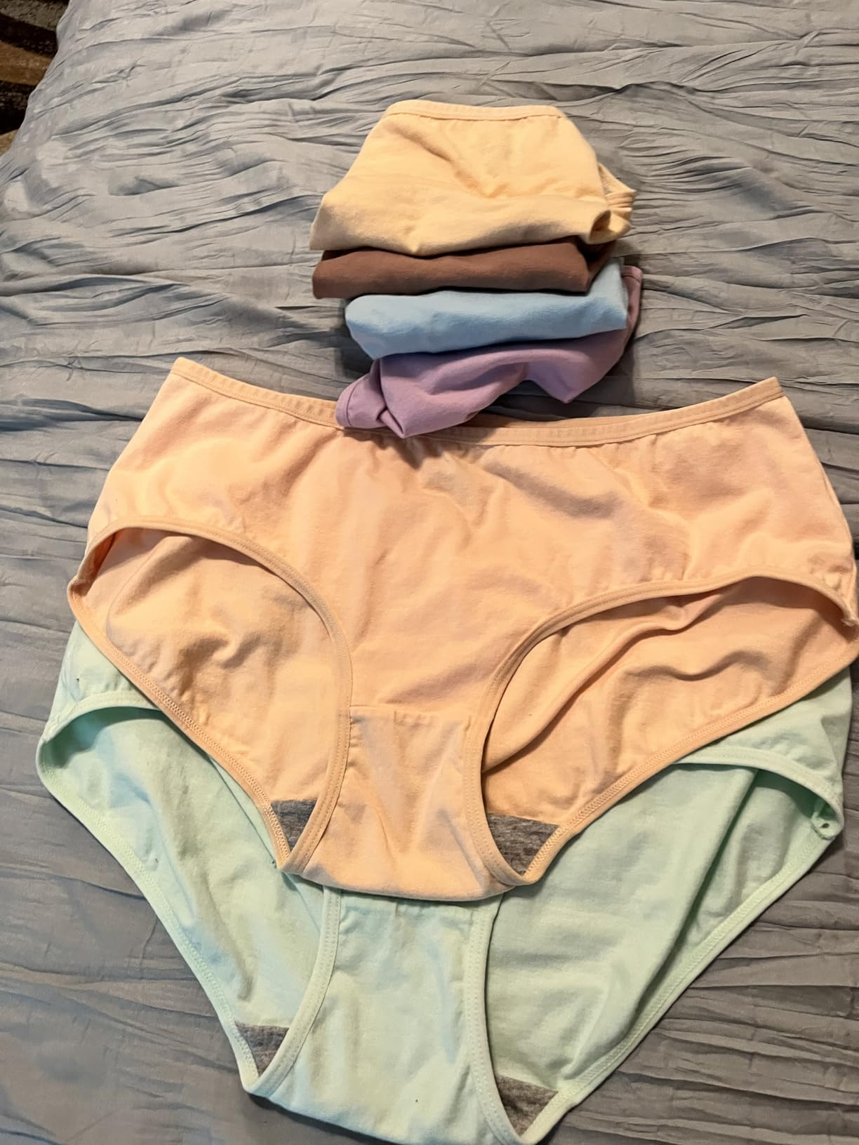 Stack of folded underwear connected  a bed, showcasing assorted  styles and textures for a buying  article