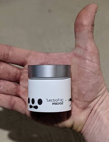 reviewer holding the mini white noise machine in the palm of their hand to show how small it is