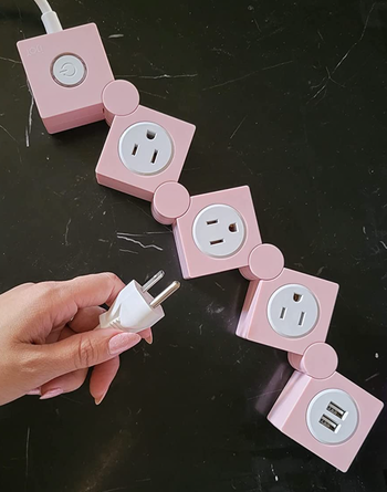 Reviewer holding pink power strip with separate squares for three outlets and two USB chargers