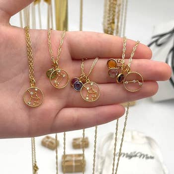 hand holding various gold necklaces with birthstones and constellations