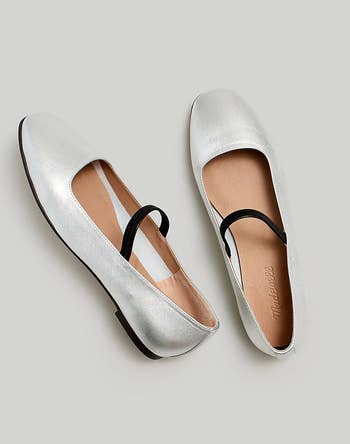 Pair of silver ballet flats with a black elastic strap 