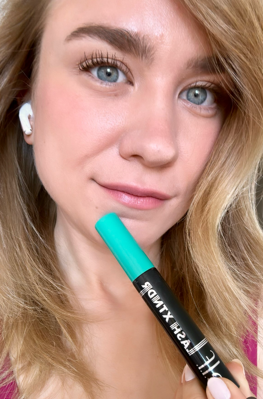 Close-up of a reviewer holding a mascara tube with fully done lashes 
