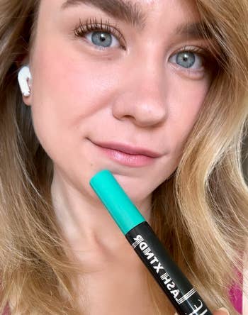 Close-up of a reviewer holding a mascara tube with fully done lashes 