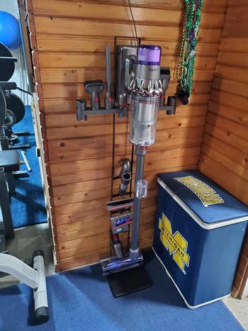Dyson vacuum mounted on a charging dock in a home gym setup next to a cooler