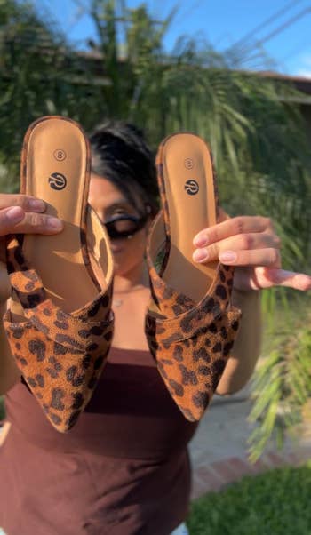 Person holding a brace of leopard people slip-on shoes