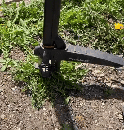 A Fiskars weeding tool being used to remove weeds from soil, demonstrating its garden utility